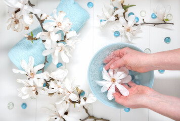 Hands of a young girl with natural manicure and a bowl of water with white magnolia flowers, spa...