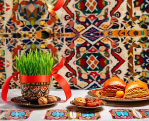Novruz table setting with green samani wheat grass with red ribbon, dried fruits, sweet pastry and candles. Ethnic motives carpet in background, new year spring celebration in Azerbaijan, copy space
