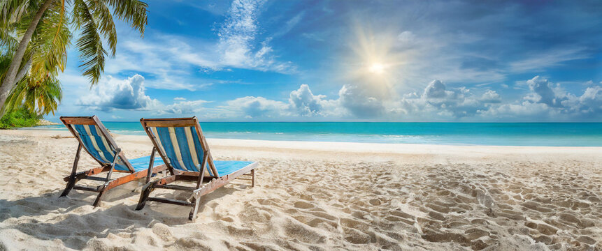 Deux chaises longues sur une plage déserte tropicale sans personne avec un ciel bleu.