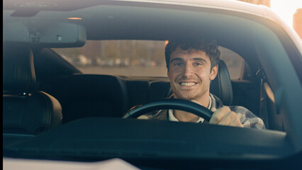 Caucasian handsome smiling man businessman sit inside modern electric car driving automobile in...