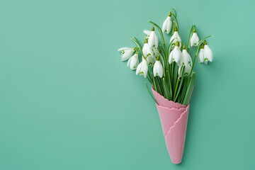 large white Snowdrop flower arrangement delicately placed inside a pink ice cream cone. The arrangement stands out against a bright green background. for various design projects, spring concepts