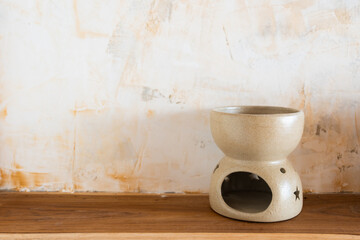 Aromatherapy oil burner with star shape cutout on ceramic design product placed on a wooden table and textured cream wall for relaxation scented at home spa