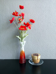 Coffee mug and red flower vase On a table with a white cement wall as a background
