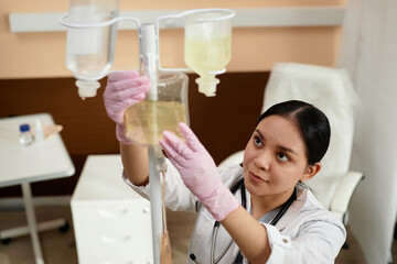 High angle portrait of female nurse setting up equipment for IV drip treatment in procedure room at clinic copy space