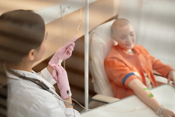 Close up of nurse setting up IV drip treatment for patient in procedure room behind glass copy space