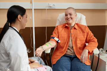 Portrait of smiling bald woman receiving chemotherapy treatment in procedure room at clinic and...