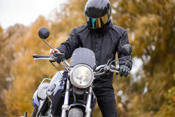motorcyclist in a motorcycle jacket and tinted helmet with a classic motorcycle in nature. Stylish...