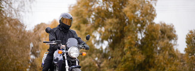 motorcyclist in a motorcycle jacket and tinted helmet with a classic motorcycle in nature. Stylish...