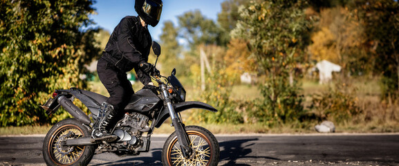 a motorcyclist wearing a helmet and motorcycle boots rides an enduro motorcycle in nature. - obrazy, fototapety, plakaty