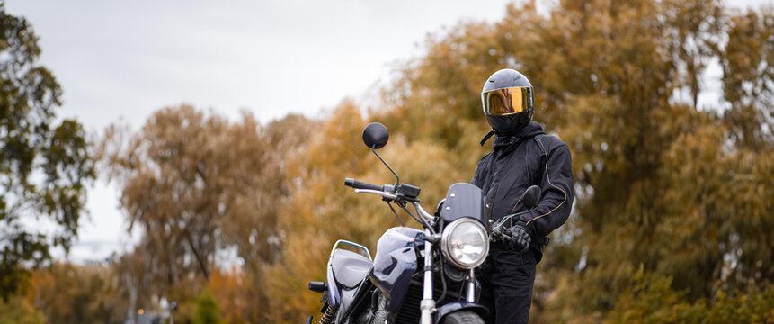 motorcyclist in a motorcycle jacket and tinted helmet with a classic motorcycle in nature. Stylish biker