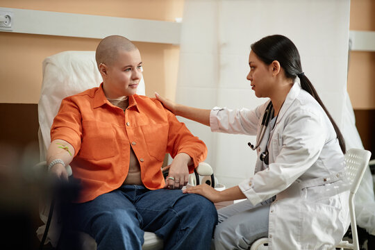 Side view portrait of young nurse comforting cancer patient receiving chemotherapy treatment in hospital