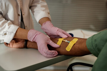 Close up unrecognizable nurse preparing patient for IV drip treatment and putting bandages on arm...