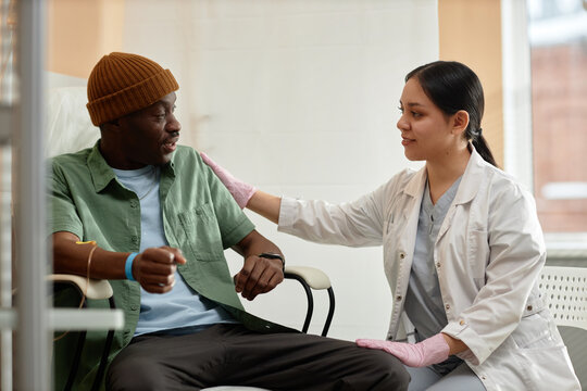 Side View Portrait Of Smiling Female Doctor Comforting Patient Receiving IV Treatment In Clinic