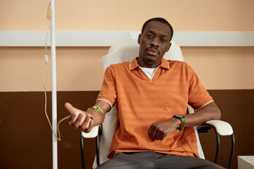 Front view portrait of African American adult man wearing mask during IV drip treatment in clinic...