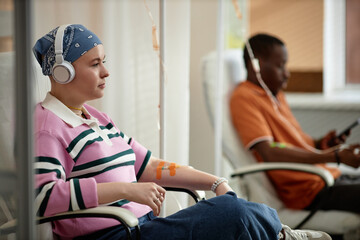 Side view portrait of two people getting chemotherapy treatment in clinic while sitting in chairs...