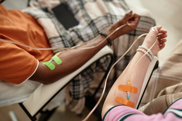 Top view closeup of two people with IV drip in arm sitting on chairs in clinic, copy space