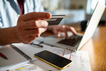 Cropped man holding a credit card using laptop at home