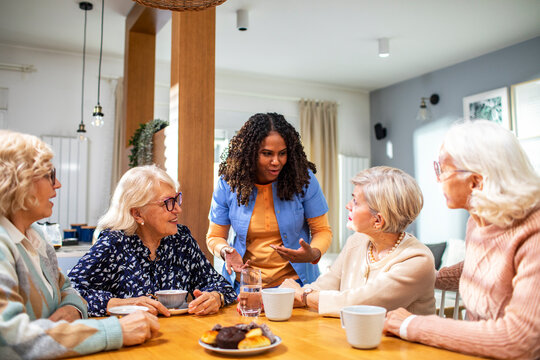 Group of senior women talking to caregiver at home kitchen table