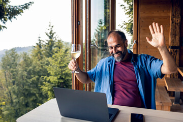 Man having a virtual toast during video call in a home with forest in the background