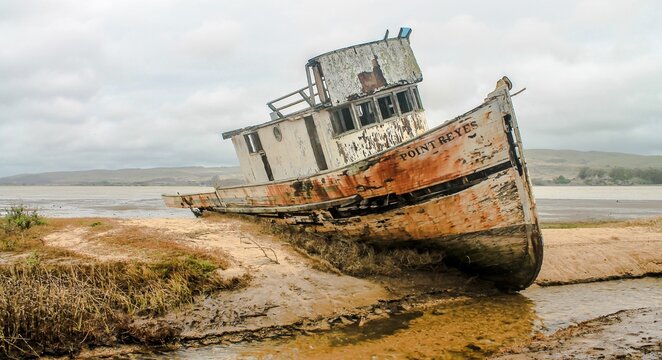 Fototapeta  A boat, overturned and washed ashore, lies on the beach, a compartment of the shoreline narrative telling a tale of challenges faced at sea.
