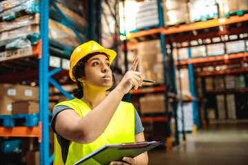 Female worker in hard hat checking inventory in warehouse