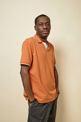 Vertical portrait of adult African American man standing in studio against beige background looking at camera