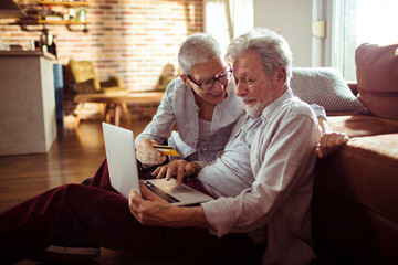 Smiling senior couple online shopping with credit card at home