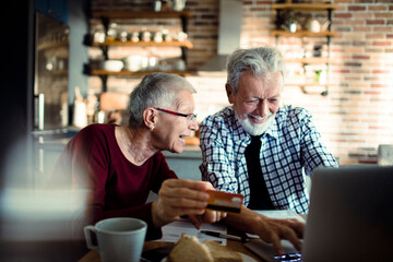 Fototapeta na wymiar Smiling senior couple using credit card on laptop at home
