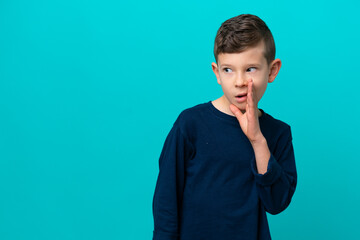 Little kid boy isolated on blue background whispering something with surprise gesture while looking to the side