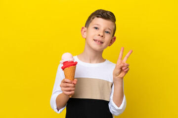 Little caucasian boy with a cornet ice cream isolated on yellow background smiling and showing...