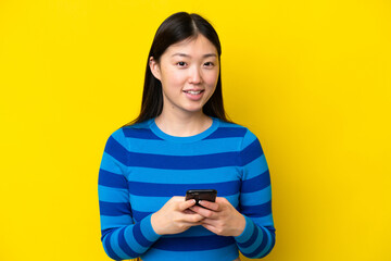 Young Chinese woman isolated on yellow background sending a message with the mobile