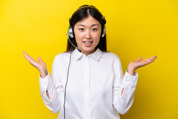 Telemarketer Chinese woman working with a headset isolated on yellow background with shocked facial...