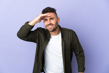 Caucasian man isolated on purple background looking far away with hand to look something
