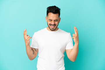 Fototapeta premium Young caucasian man isolated on blue background with fingers crossing