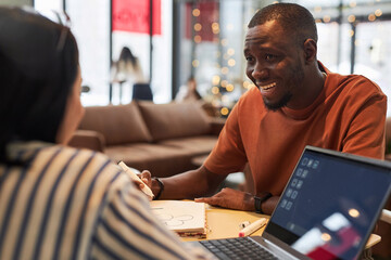 Portrait of two young people in business meeting at coffee shop focus on smiling Black man talking...