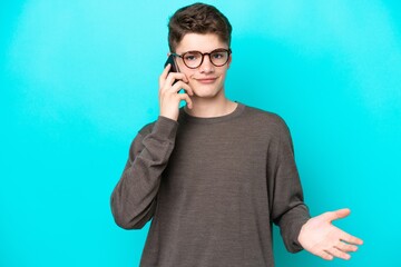 Teenager Russian man isolated on blue background keeping a conversation with the mobile phone with someone