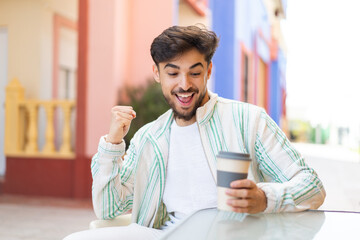 Handsome Arab man holding a take away coffee at outdoors celebrating a victory