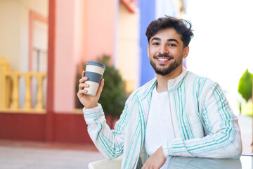 Handsome Arab man holding a take away coffee at outdoors smiling a lot