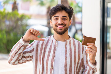 Handsome Arab man holding a wallet at outdoors proud and self-satisfied