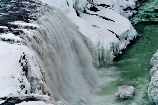 Icy waterfall with snow-covered rocks and vibrant turquoise water, showcasing the beauty of winter. Location: Gullfoss Falls, Iceland.