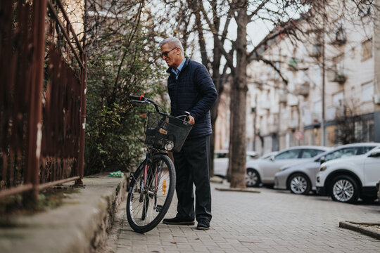 Senior man pausing with a bicycle on an urban street in daylight.