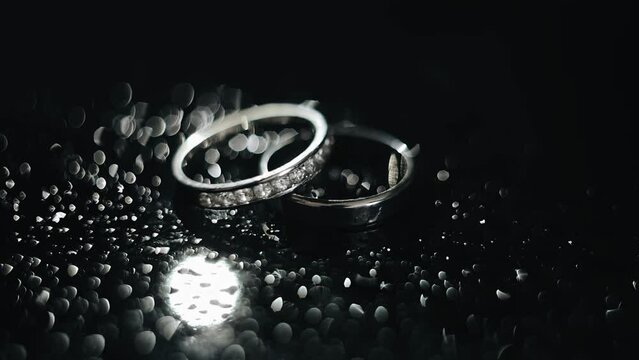 The light illuminates two silver rings lying on a dark surface. The rings cast beautiful highlights