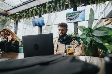 Focused young professionals engaged in their work at laptops in a cozy, plant-filled urban coffee shop setting. Collaboration and entrepreneurship concept.