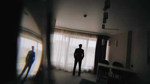 A man stands in front of the window and looks towards the window. Cool silhouette in the room