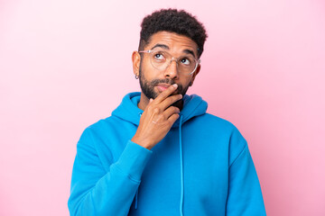 Young Brazilian man isolated on pink background With glasses and having doubts