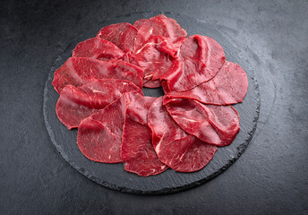 Traditionelle Carpaccio vom Rind serviert als Draufsicht auf einer schwarzen Design Platte mit...