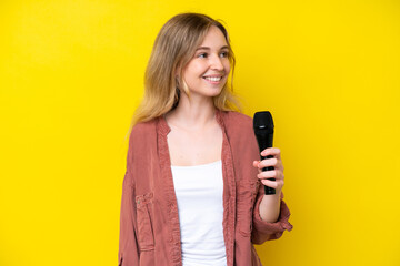 Young singer caucasian woman picking up a microphone isolated on yellow background looking side