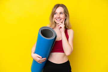 Young sport caucasian woman going to yoga classes while holding a mat isolated on yellow background...