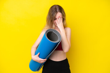 Young sport caucasian woman going to yoga classes while holding a mat isolated on yellow background...
