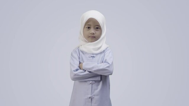 Muslim little girl wearing a hijab crosses her arms. Happy female kid posing indoor in a muslim outfit